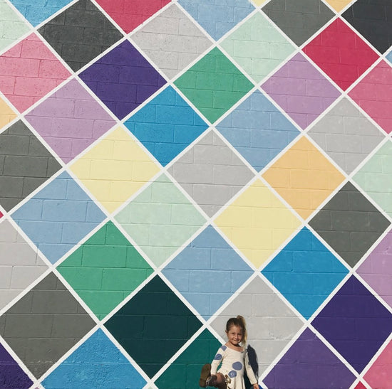 A large colorful murals made composed of tilted squares in an array of bright colors.  A little girl is standing in front of the mural.